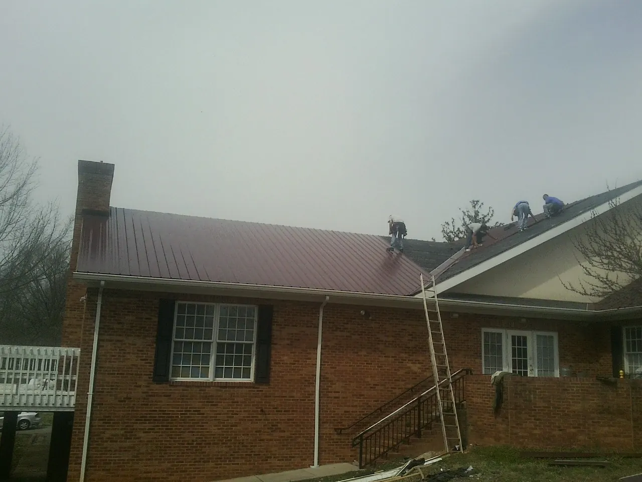 Crew setting red metal roofing panels on a brick home in Hanover